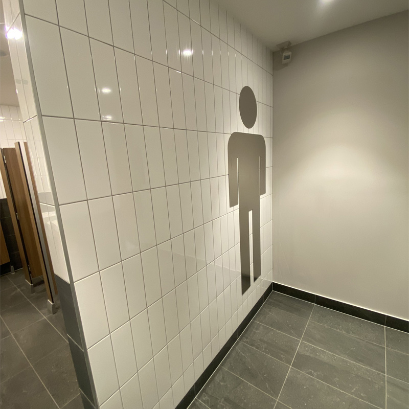 White wall tiles with a men's toilet symbol above grey floor tiles