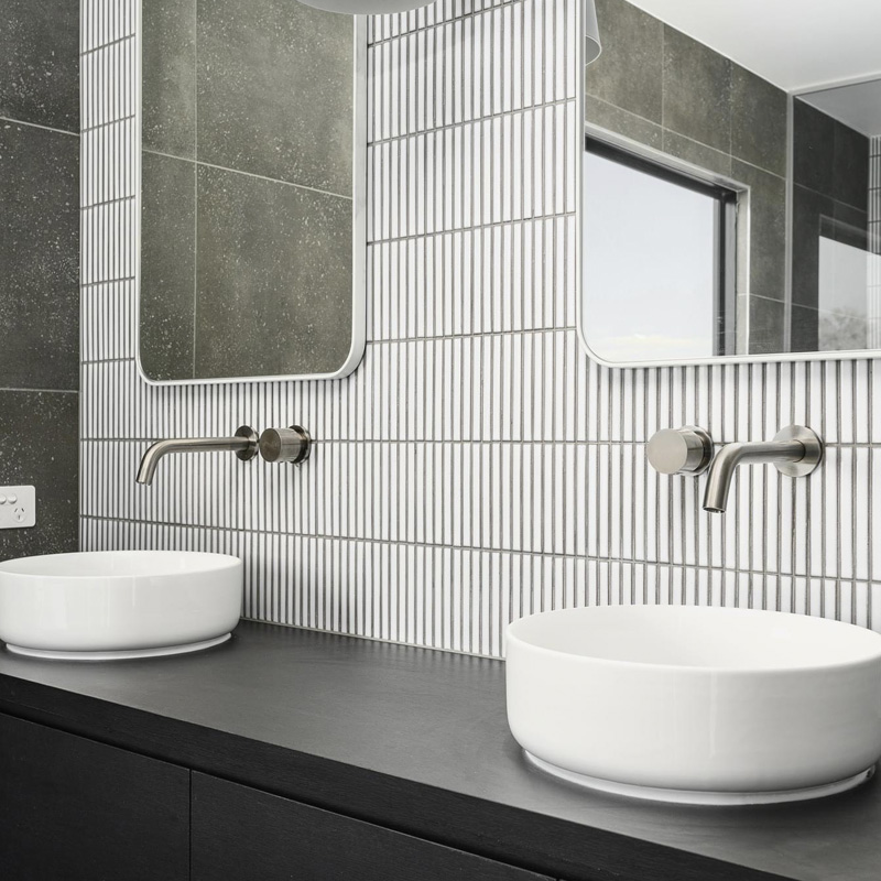 Two vessel basins on a black vanity against white finger tiles