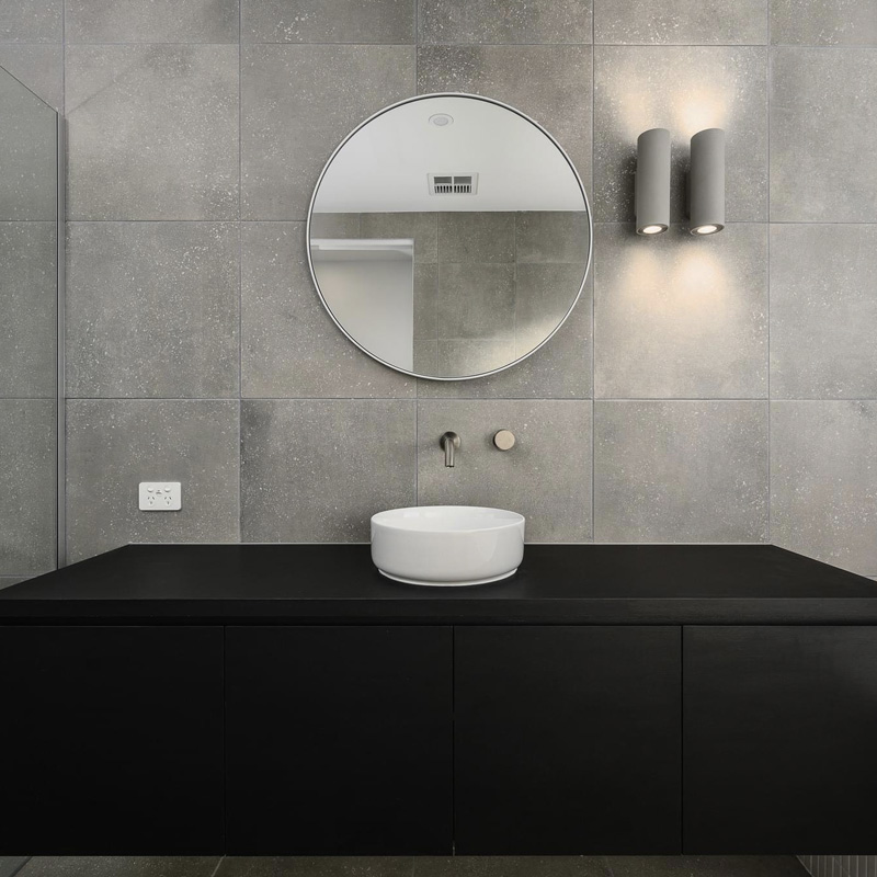 Black vanity with a round mirror and vessel basin against large grey tiles