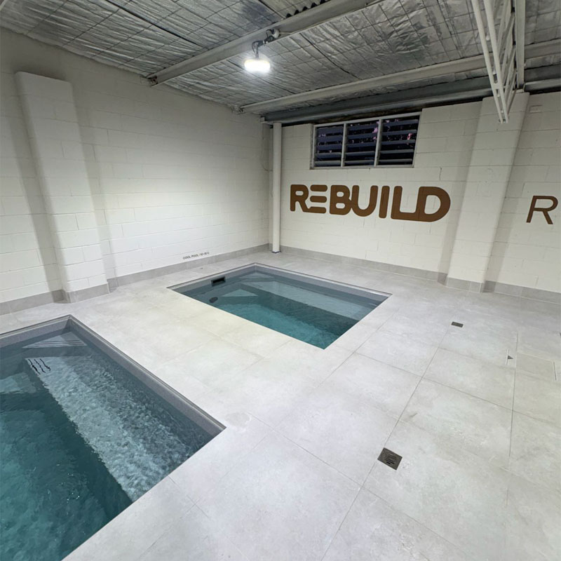 Pale tiled floor between two plunge pools below a Rebuild wall sign